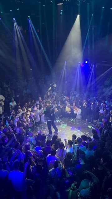 A performer surrounded by a crowd beneath blue nightclub lights.