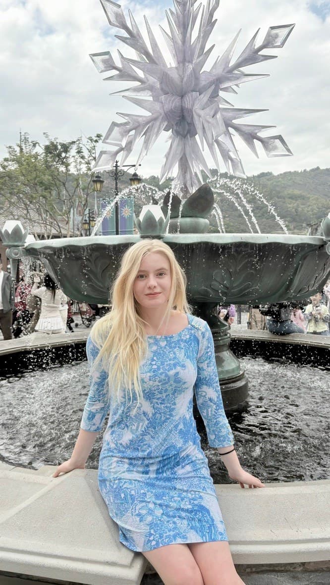Hannah in a blue dress beside a snowflake fountain on her Disney trip in Japan.