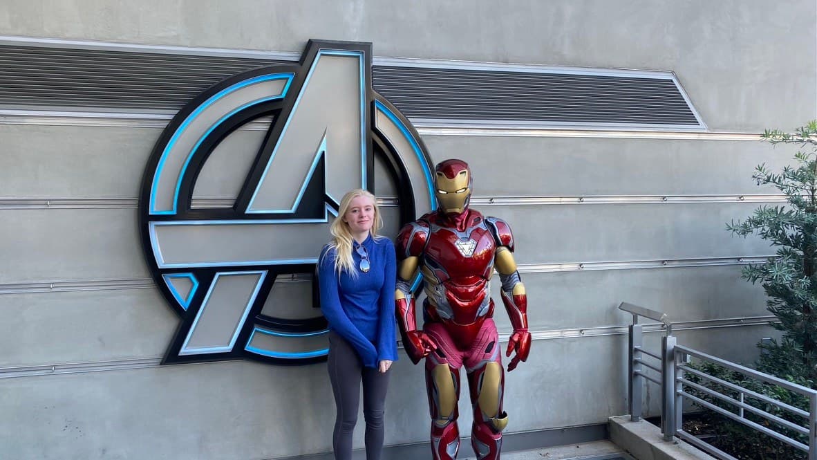 Hannah beside Iron Man in front of the Avengers emblem at Disney California Adventure.