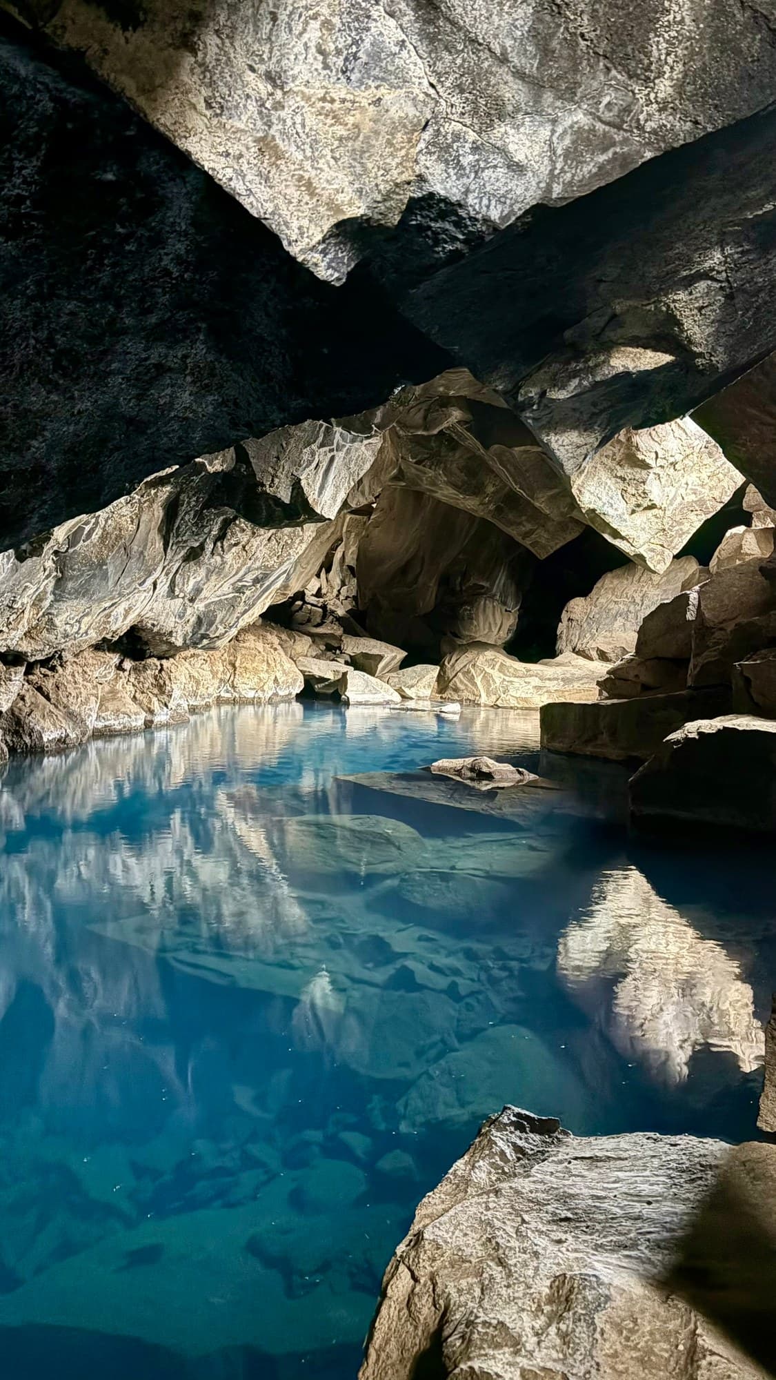 Clear blue geothermal water reflecting the angular lava-rock walls inside Grjótagjá cave in North Iceland.