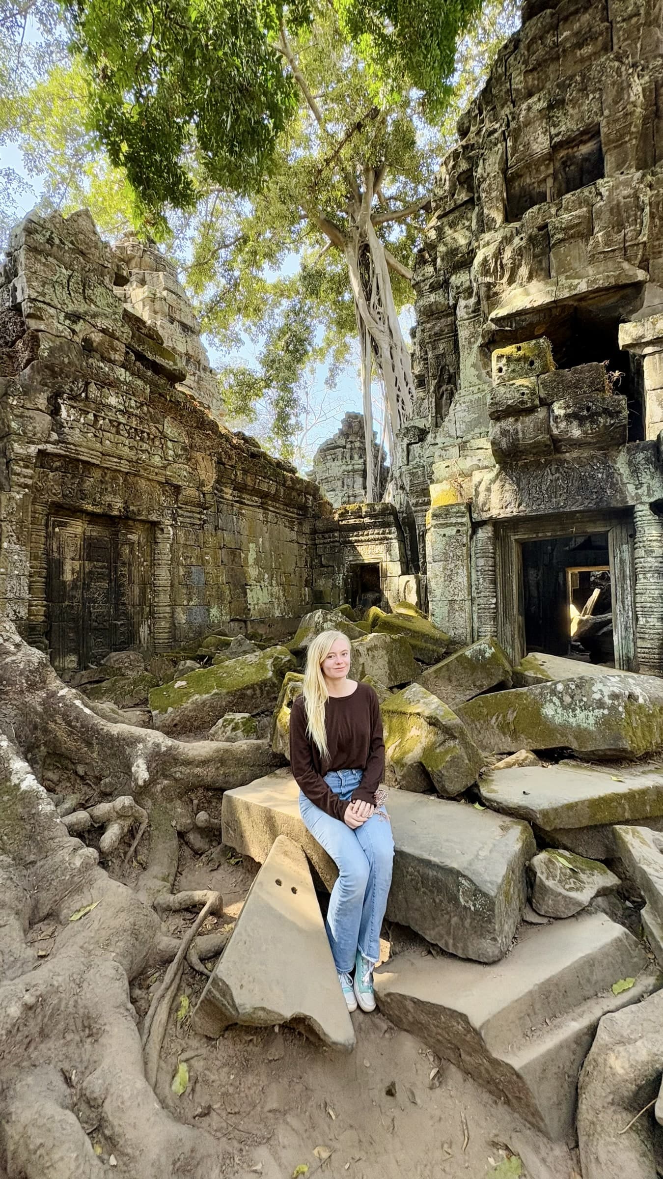 Hannah sitting on a stone ledge among weathered ruins and tree roots