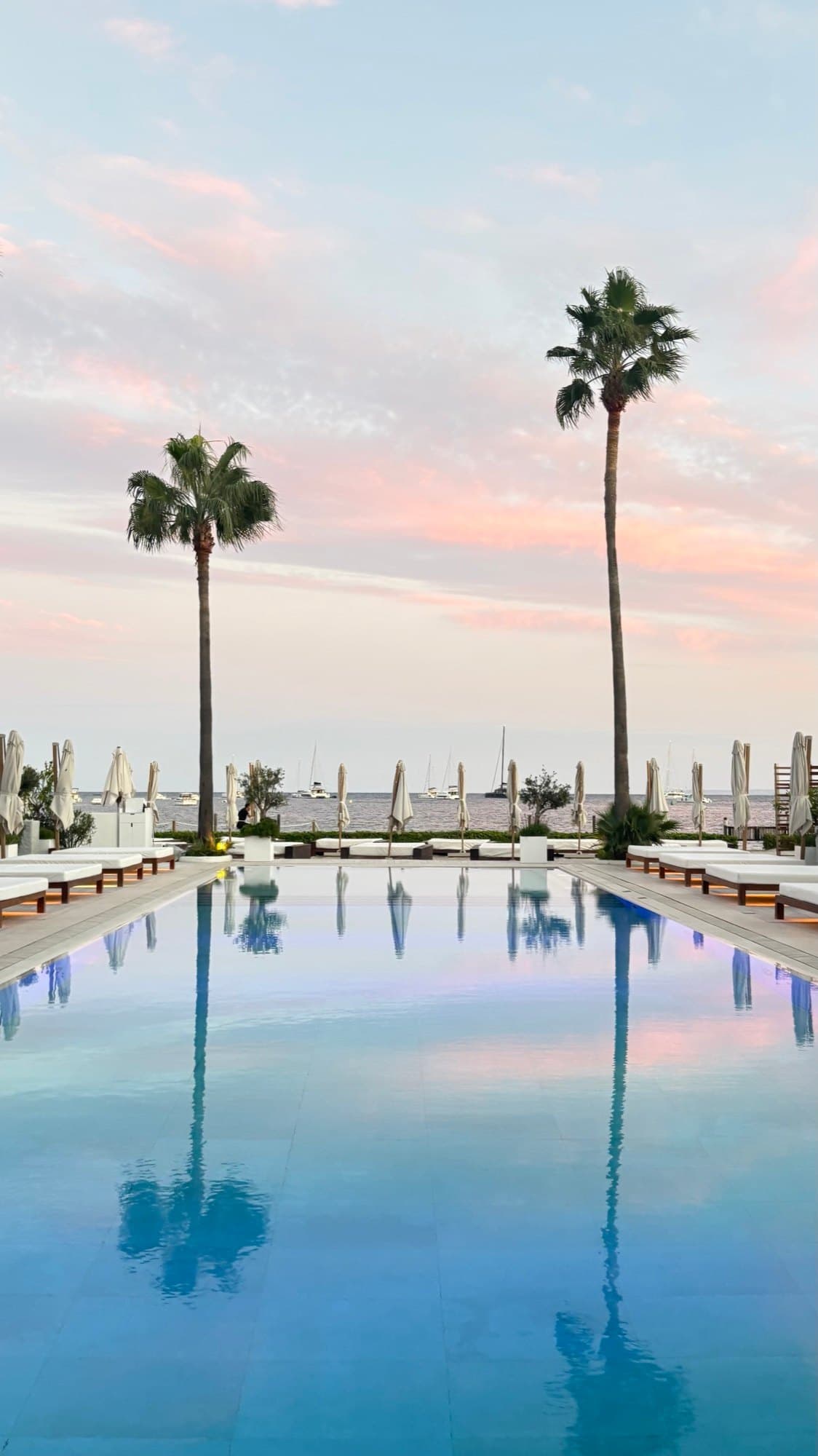 Palm trees and a pink evening sky reflected in a pool overlooking the sea in Ibiza.