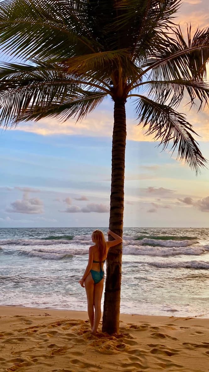 Hannah beside a palm tree on the beach at Meliá Vinpearl Phu Quoc in the evening light.
