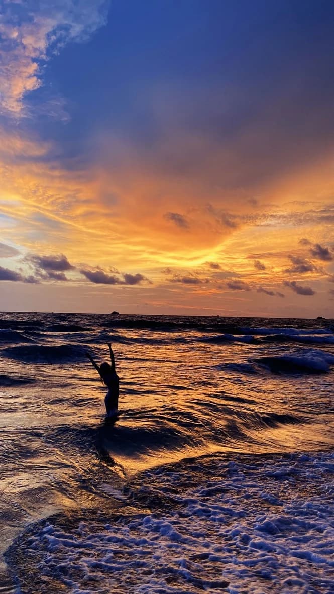 Hannah silhouetted in the sea beneath a gold and orange sunset at Meliá Vinpearl Phu Quoc.