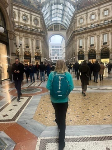 Hannah carrying a compact turquoise backpack through a glass-roofed shopping arcade.