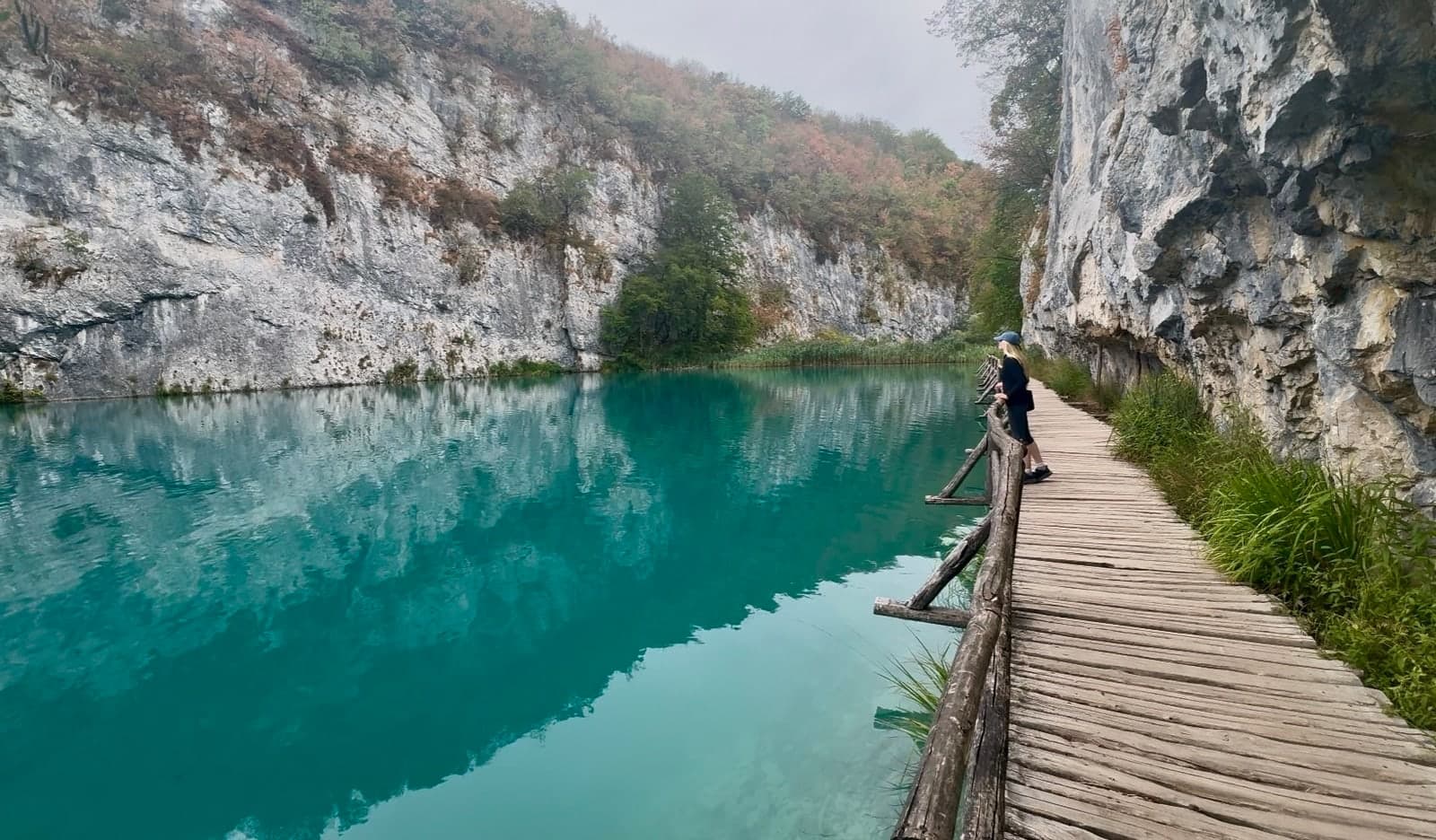 Hannah on a curving boardwalk beside turquoise water and limestone cliffs at Plitvice Lakes